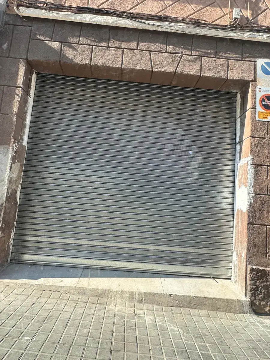 Persiana metálica cerrada en la fachada de un local con piedra