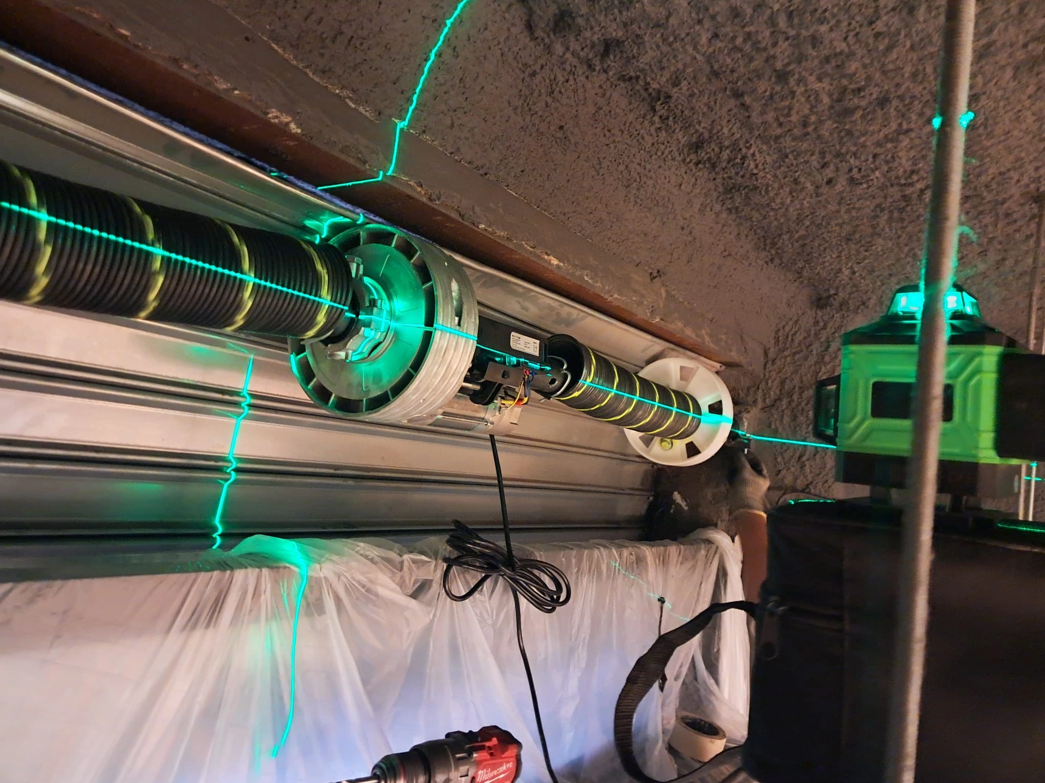 Instalación y alineación con nivel láser verde del eje y tambor en puerta de garaje.