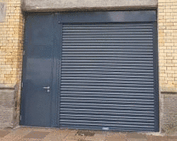 Instalación de persiana de seguridad ciega con puerta de paso incorporada para local comercial.