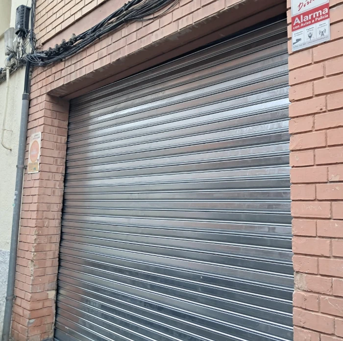 Instalación de persiana metálica enrollable gris en acceso de local urbano.
