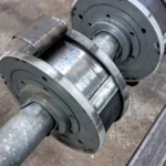 Conjunto de rodillos industriales metálicos montados en un eje, con desgaste visible.