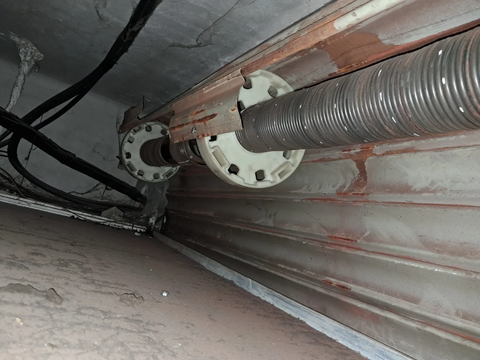 Muelle de torsión de persiana enrollable montado en eje, con piezas y cableado visibles.