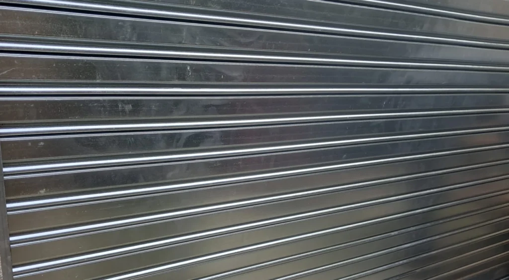 Persiana metálica enrollable cerrada con candado en la parte inferior y entorno de almacén. Tipos de lamas. Blogs