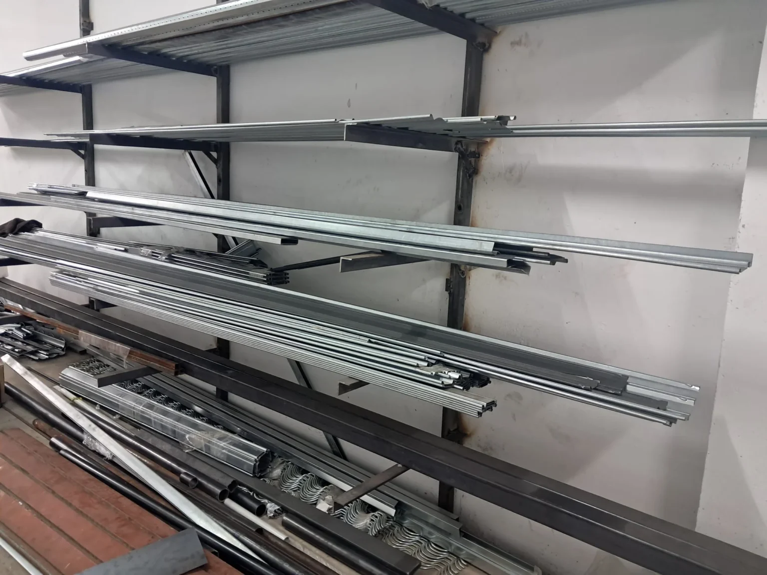 Estantería de pared con perfiles y barras metálicas apiladas y organizadas en un taller.