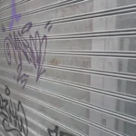 Persiana metálica perforada en primer plano, cubierta de grafiti en morado y negro.