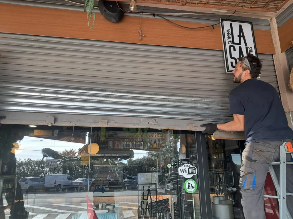 Técnico subido a una escalera levantando la persiana metálica de un local