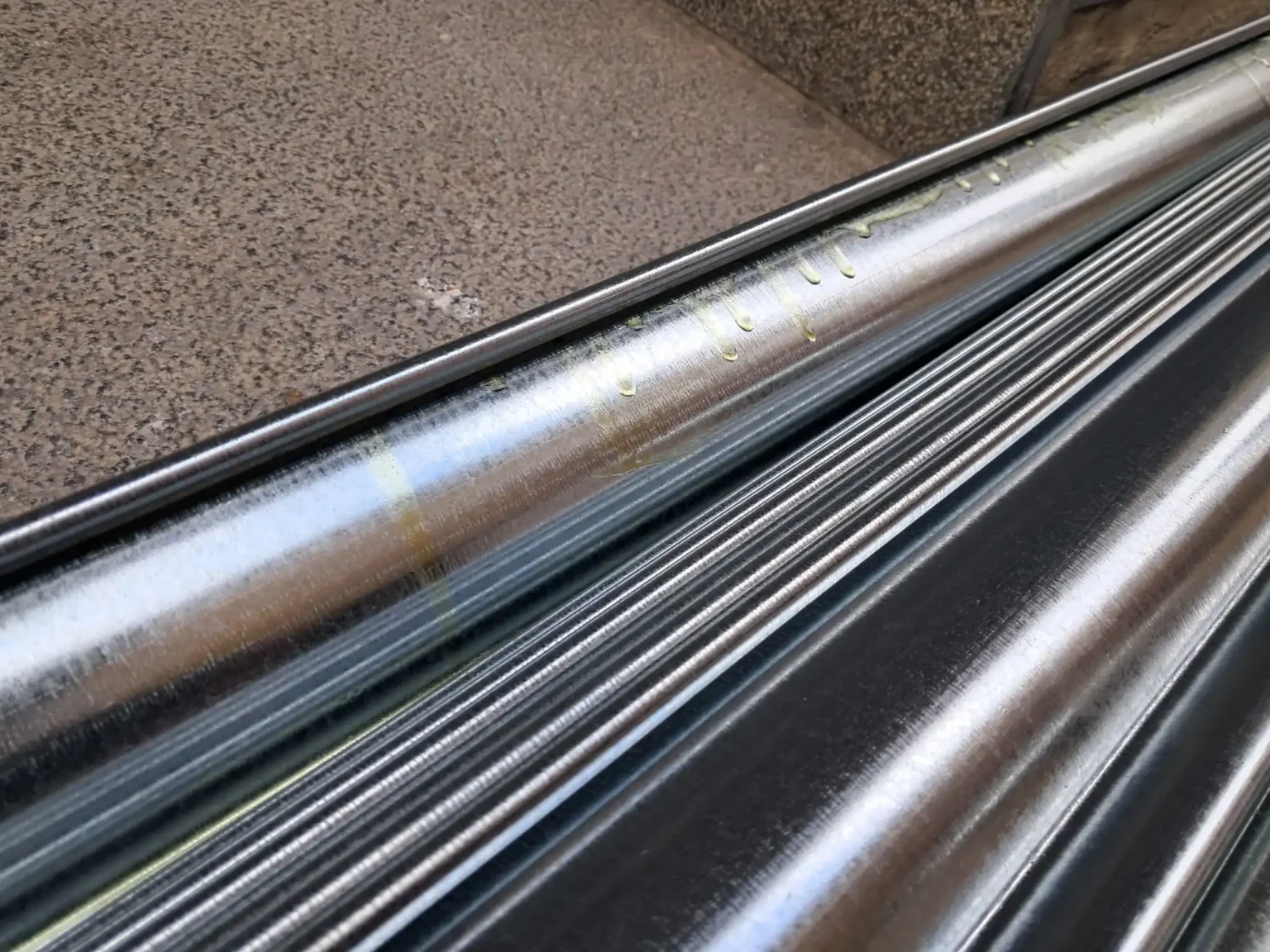 Tuberías metálicas brillantes apiladas diagonales, reflejos de luz y fondo de superficie rugosa de concreto.