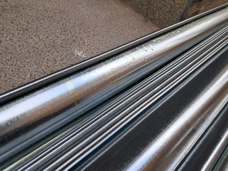 Tuberías metálicas brillantes apiladas diagonales, reflejos de luz y fondo de superficie rugosa de concreto.