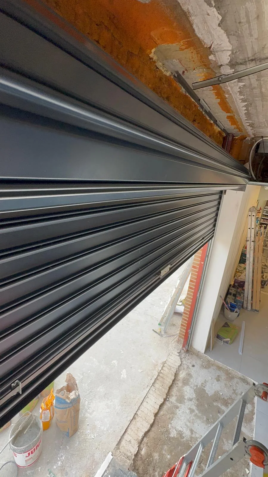 Servicio de instalación de persiana metálica enrollable en local comercial, abierta a media altura.