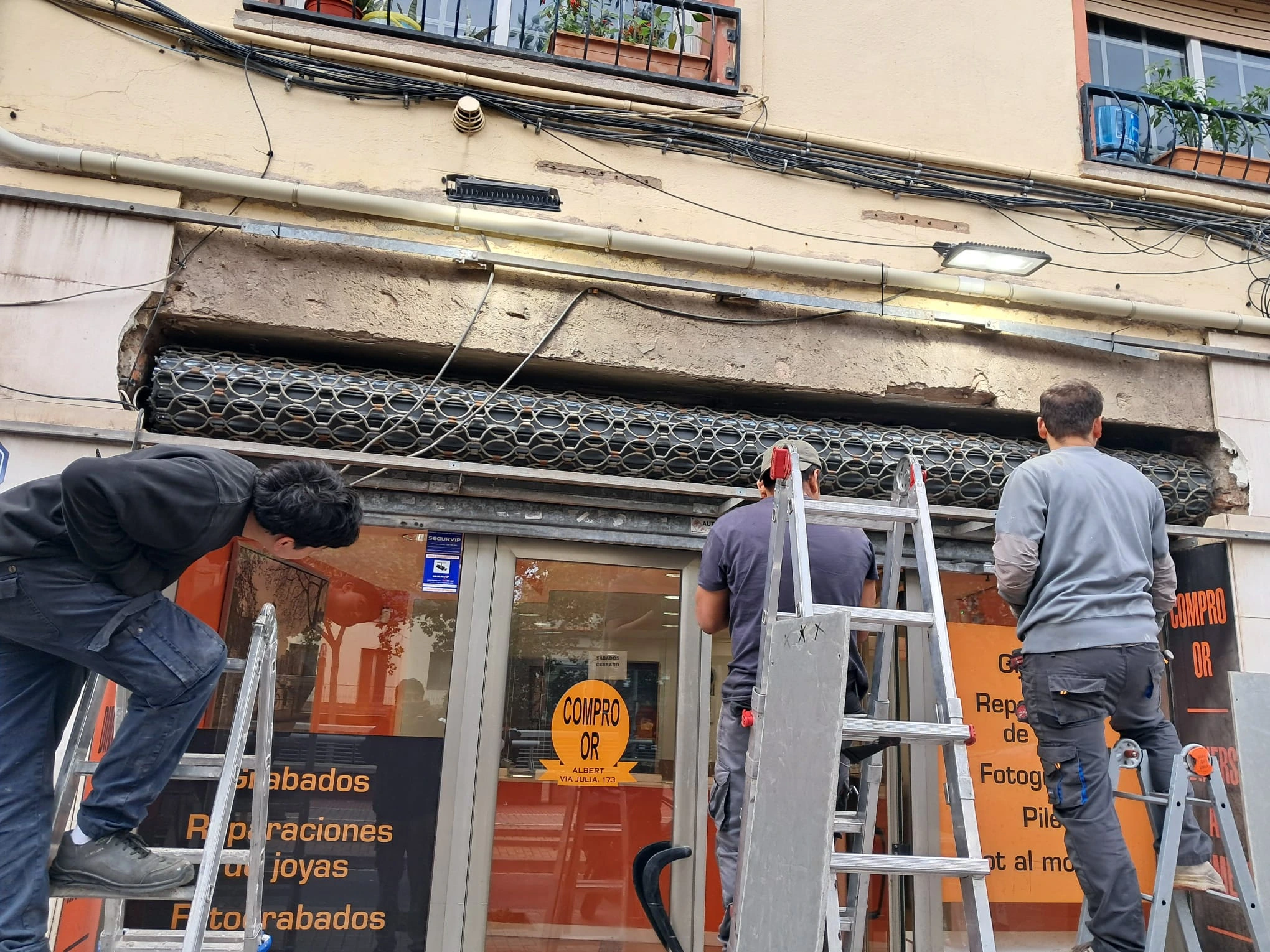 Técnicos especialistas reparando una persiana de seguridad metálica en la entrada de una tienda.