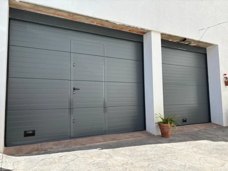 Puerta seccional gris automática para garaje moderno con paneles aislantes y apertura vertical.