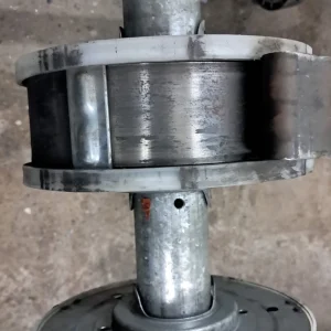 Detalle de una pieza de mantenimiento de persianas: un eje metálico con óxido visible y dos rodillos plásticos desgastados en los extremos.