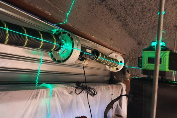 Instalación y alineación con nivel láser verde del eje y tambor en puerta de garaje.