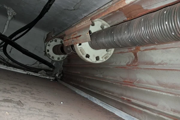 Detalle de muelle de torsión montado en eje de persiana con sistema de poleas y cableado técnico.
