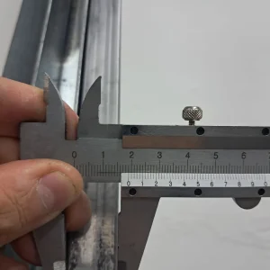 Calibrador vernier midiendo el ancho de una pieza metálica, lectura alrededor de 26 mm.