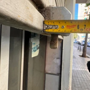 Cinta métrica midiendo una barra metálica oxidada junto a una ventana en la calle.