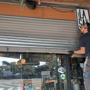 CONTACTO ​- Técnico subido a una escalera levantando la persiana metálica de un local