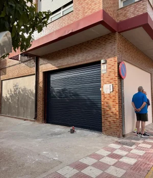 Puerta enrollable automática instalada en fachada de piedra con acceso estrecho.