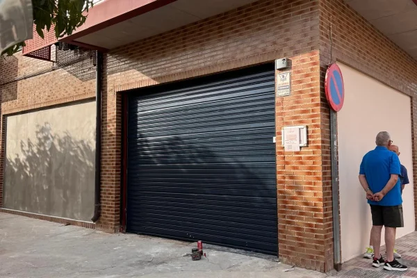 Puerta enrollable automática instalada en fachada de piedra con acceso estrecho.