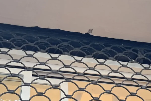 Reja decorativa de hierro forjado instalada bajo cornisa para seguridad elegante de ventanas residenciales o comerciales.